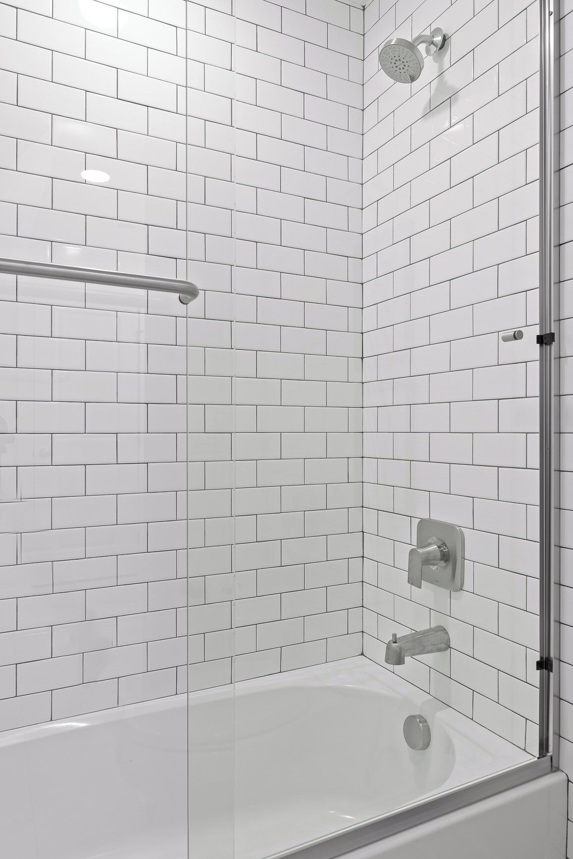 A modern bathroom with white subway tiles, a glass shower enclosure, a bathtub, and a handheld showerhead.