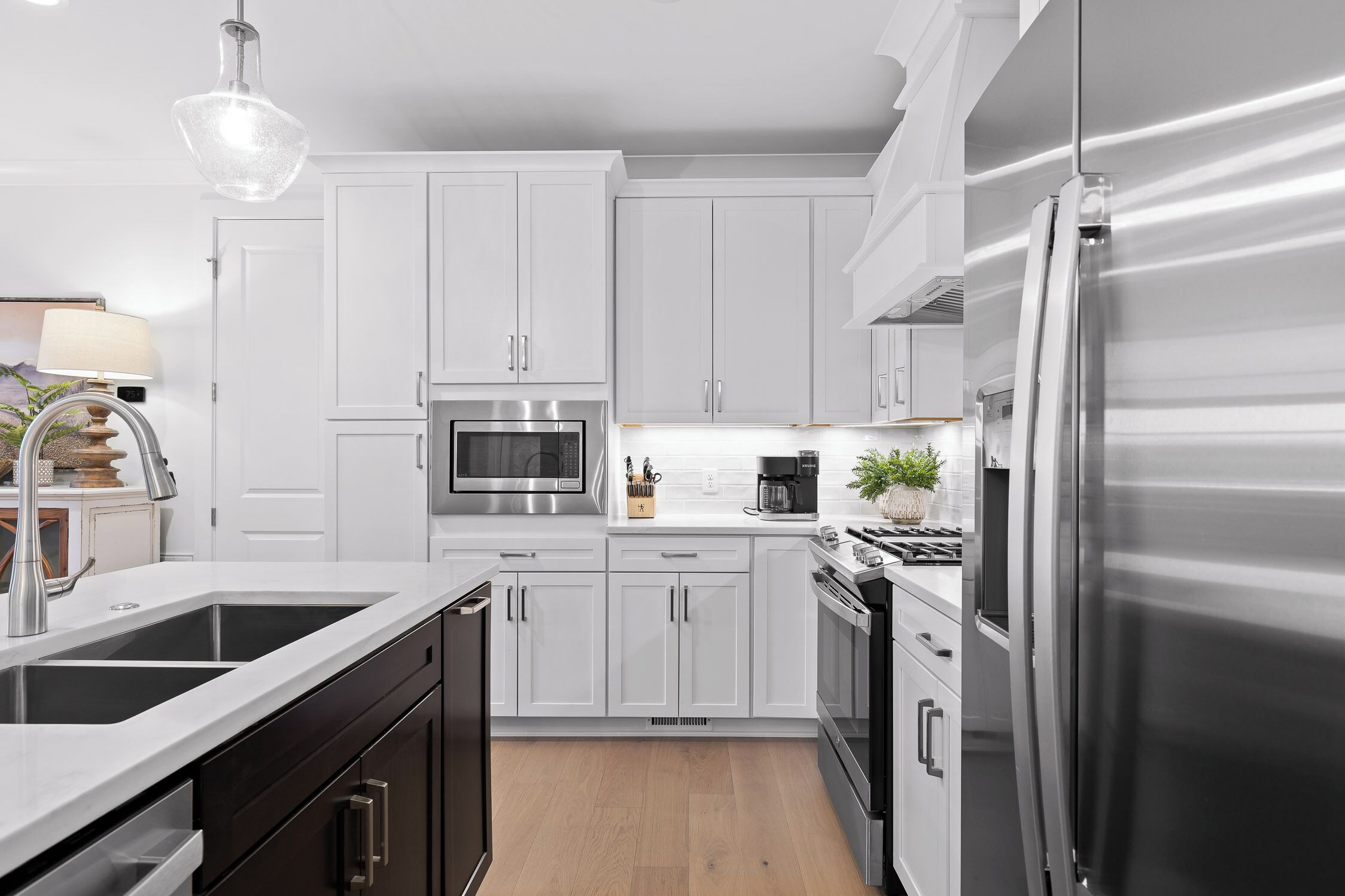 A modern kitchen with white cabinetry, stainless steel appliances, and a wooden floor.
