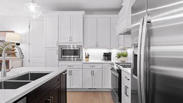 A modern kitchen with white cabinetry, stainless steel appliances, and a wooden floor.