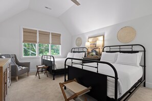 Ein Schlafzimmer mit einem Bett, einem Sessel, einem kleinen Tisch und einem Fenster mit Jalousien.