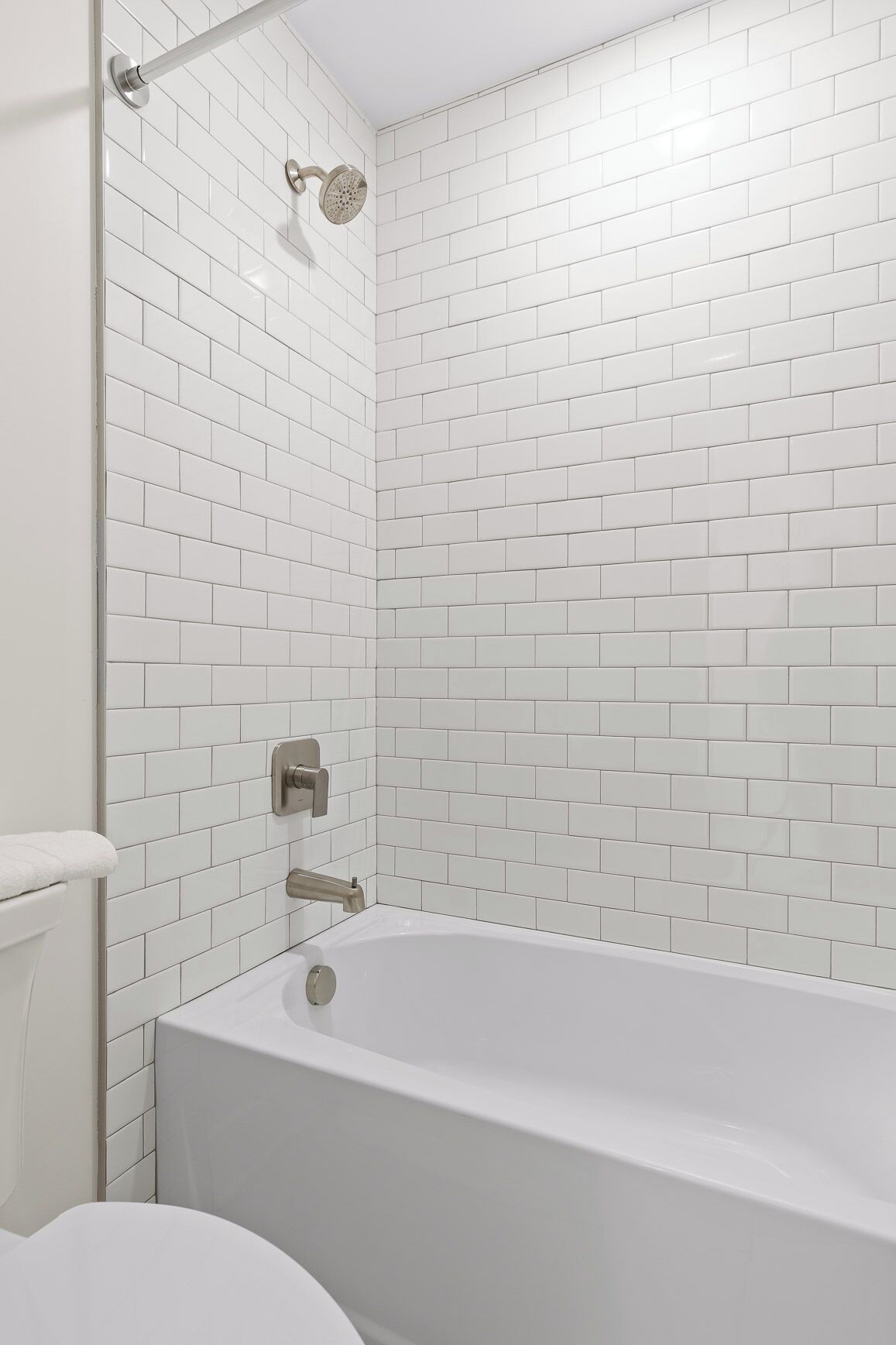 A bathroom with white subway tiles, a bathtub, and a shower with a handheld showerhead.