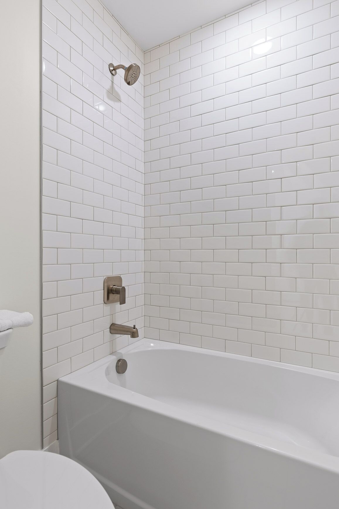 Ein Badezimmer mit weißen Fliesen, einer Badewanne und einer Duschbrause.