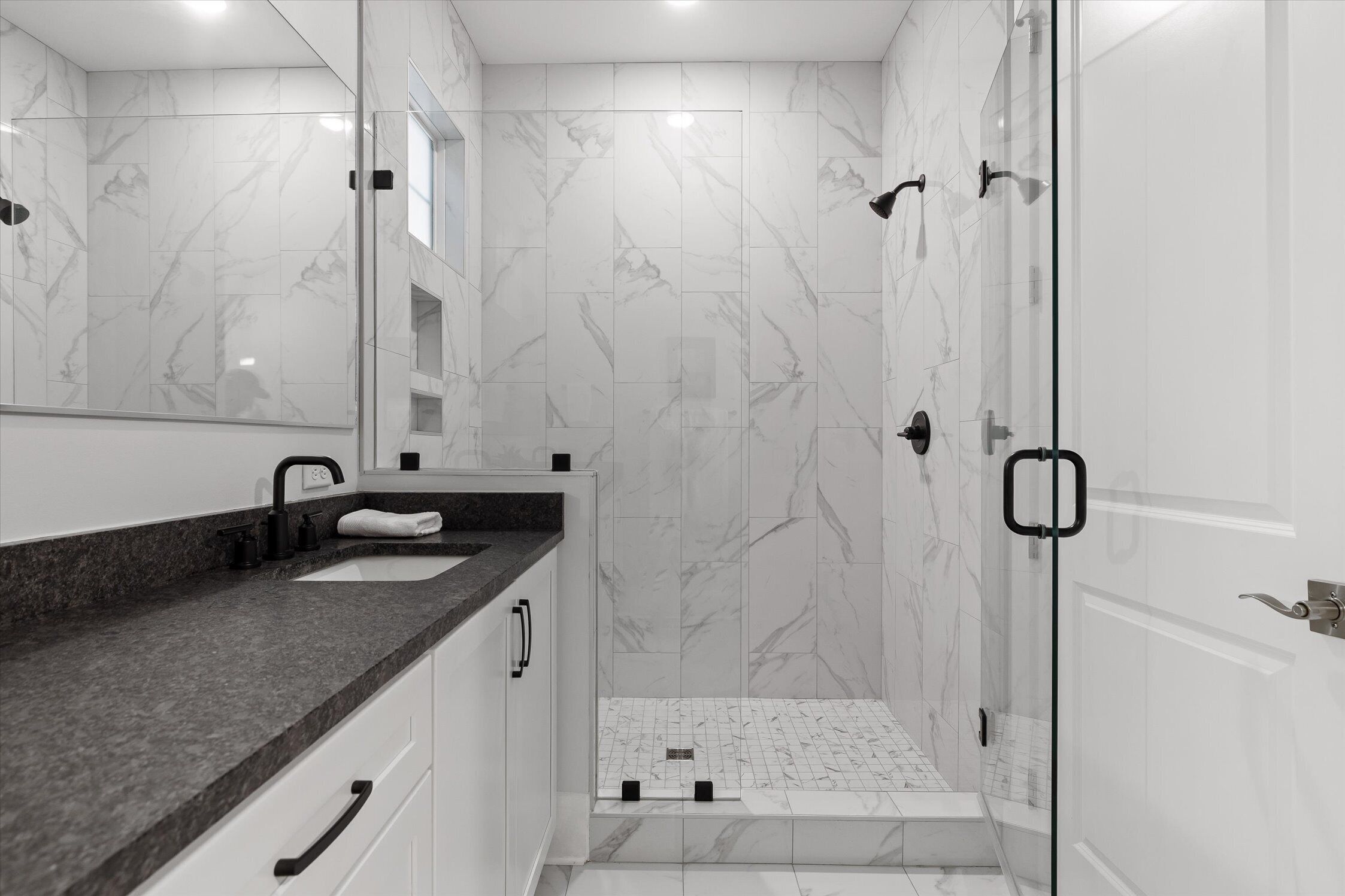A modern bathroom with a glass shower enclosure, a double sink vanity, and marble tiles.