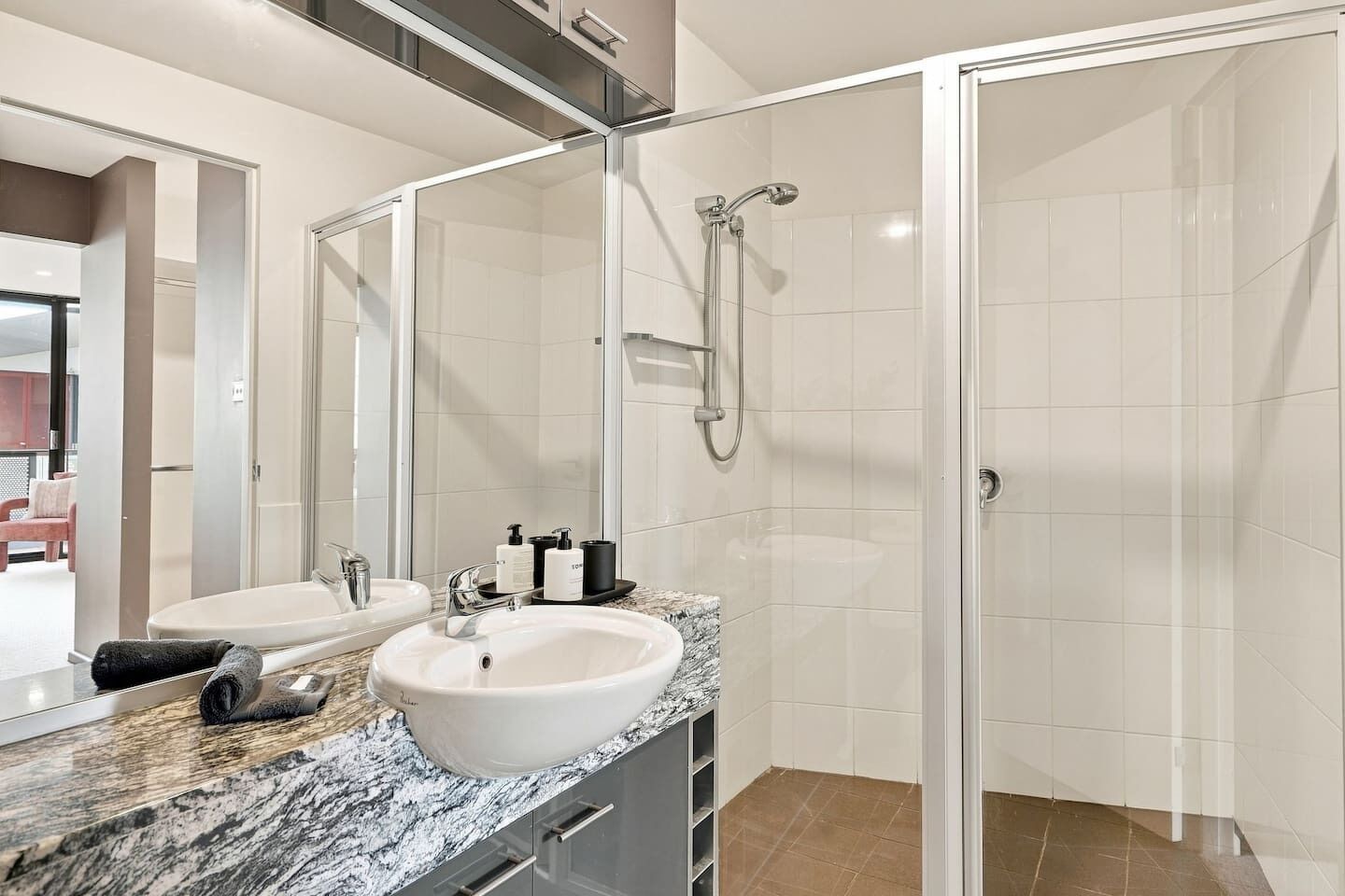 A modern bathroom with a glass-enclosed shower, two sinks, and a marble countertop.
