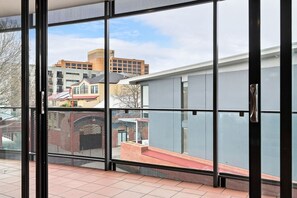 A view through a glass door with a metal handle, leading to a balcony with a tiled floor.