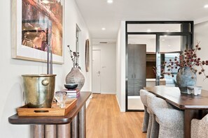 Un interior moderno con una mesa de comedor de madera, un florero con ramas secas y un cuadro abstracto grande en la pared.