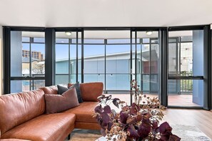 Una sala de estar moderna con un sofá de cuero, una planta decorativa y ventanas amplias con vistas a la ciudad.