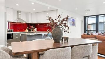 A modern kitchen with white cabinets, a red backsplash, and a central island. There is a dining table with chairs in the foreground.