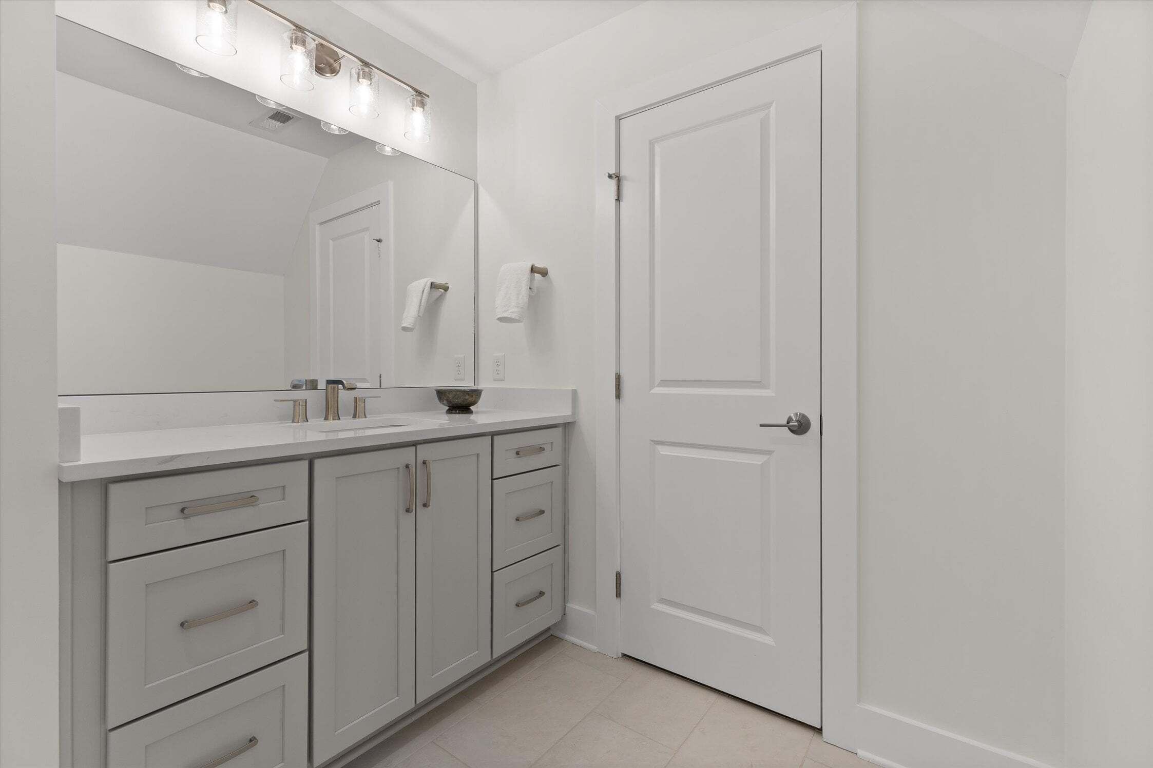 A bathroom with a white vanity, a mirror, a towel rack, and a door.