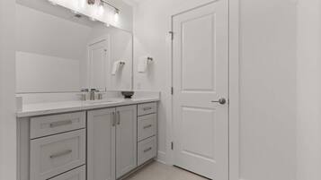 A bathroom with a white vanity, a mirror, a towel rack, and a door.