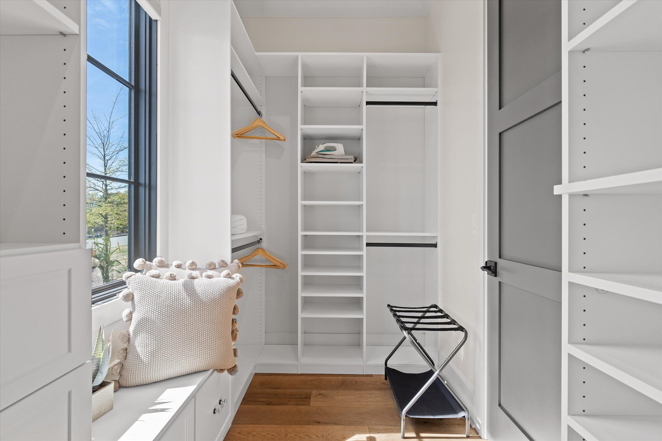 A walk-in closet with white shelving, a wooden hanger, and a black metal rack.