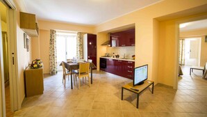 Amplia sala de estar con mesa de comedor, sillas, televisor y cocina con armarios rojos.