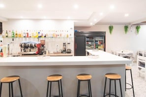 Zona de bar con taburetes, una máquina de café y una variedad de botellas en estantes.