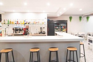 Zona de bar con taburetes, una máquina de café y una variedad de botellas en estantes.