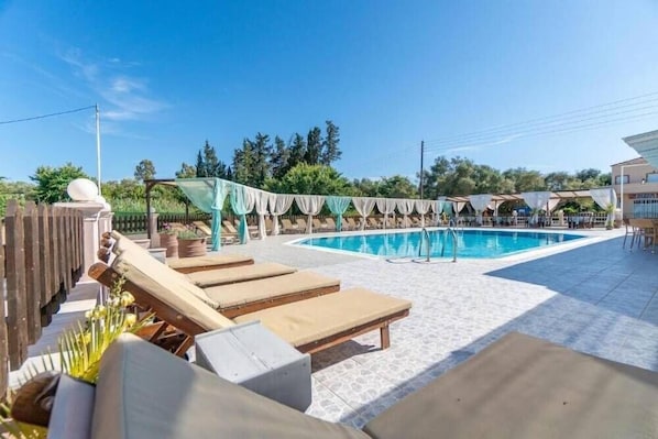 Zona de piscina con sillas de descanso y un área de estar cubierta.