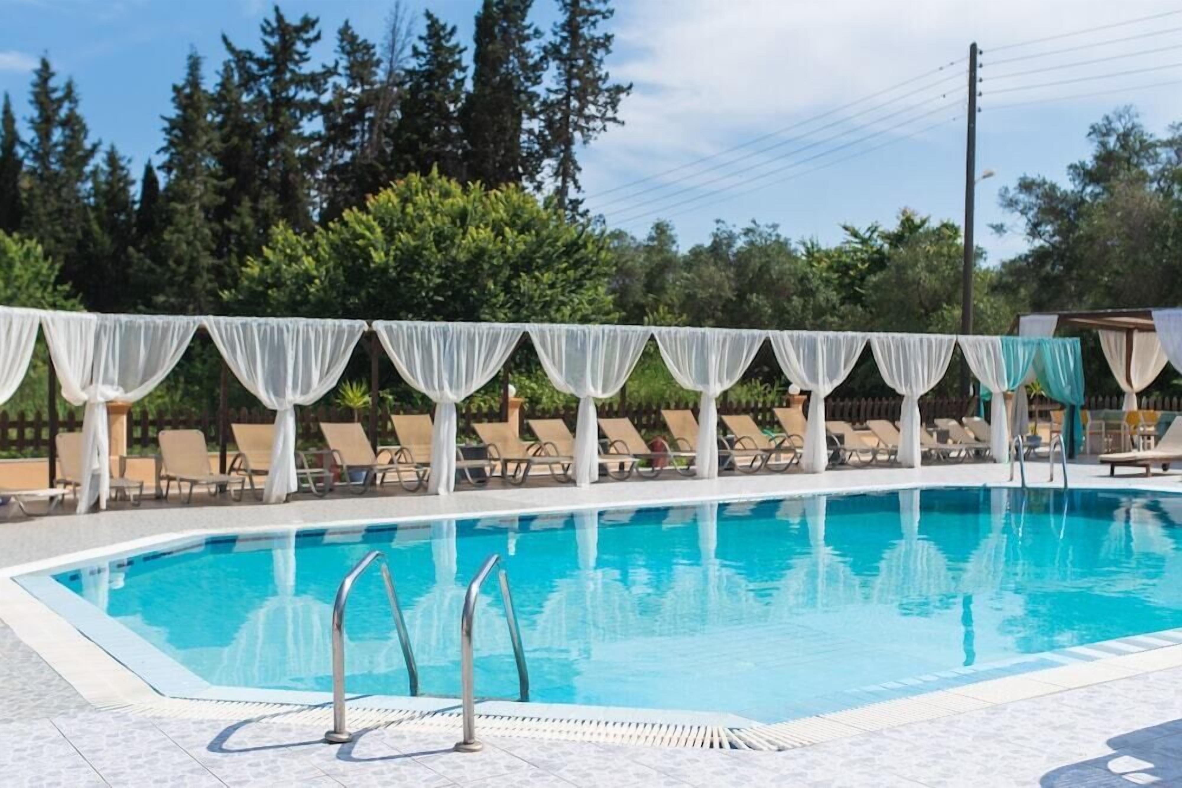 Une piscine à l’eau d’un bleu cristallin, entourée de chaises longues et de tentures blanches.