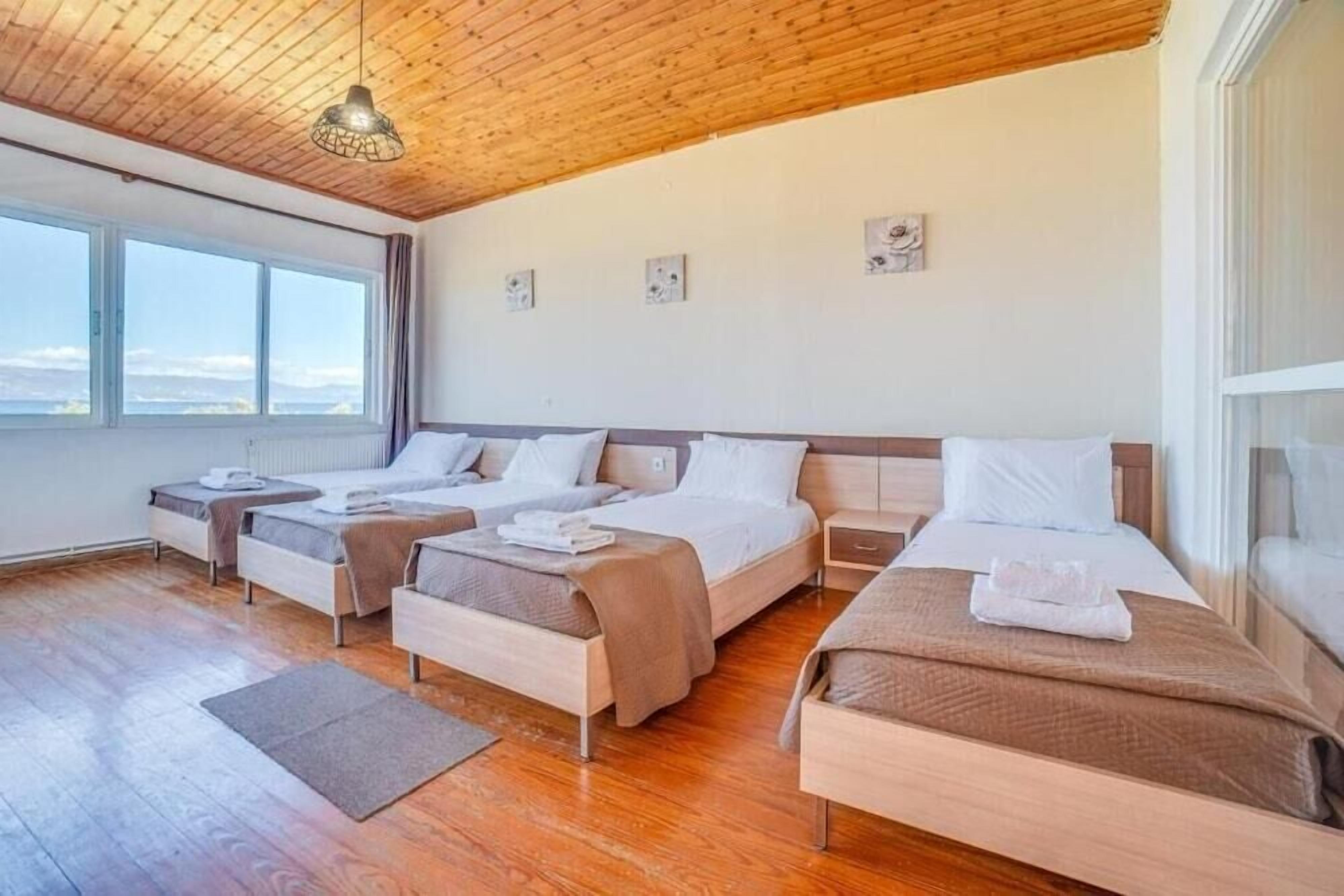 Ein Hotelzimmer mit drei Betten, Holzboden, einem großen Fenster und einer Holzbalkendecke.