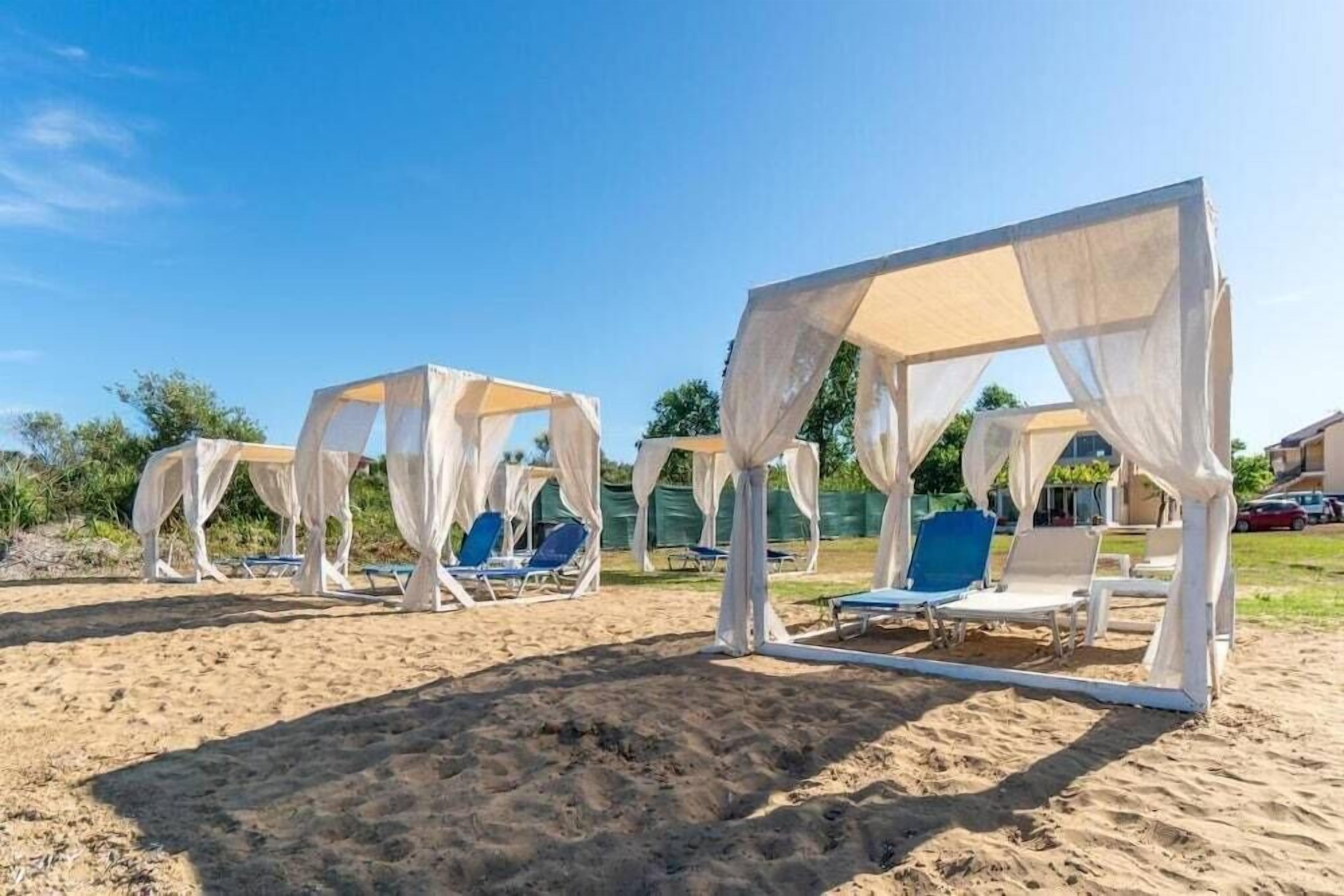 Ein Strandbereich mit weißen Sonnensegeln und blauen Liegestühlen.