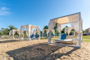A beachside area with white canopies and blue lounge chairs. - Saint Peter Bay Aparthotel (Corfu)