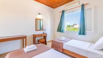Ein Hotelzimmer mit zwei Betten, einem Schreibtisch, einem Stuhl, einem Spiegel und einem Fenster mit Vorhängen.