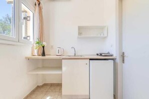 Una cocina compacta con lavavajillas integrado, una ventana pequeña con cortinas y un estante sobre el fregadero.