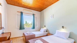 Un dormitorio con dos camas, techo de madera, una ventana con cortinas y una mesita de noche con lámpara.