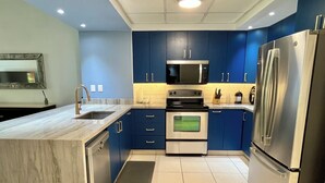 A modern kitchen with blue cabinets, stainless steel appliances, and a marble countertop. - Playa Royale Beachfront Family Condo °BBQ, Terrace & Garden Views° (Nuevo Nayarit)