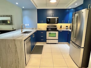 A modern kitchen with blue cabinets, stainless steel appliances, and a marble countertop. - Playa Royale Beachfront Family Condo °BBQ, Terrace & Garden Views° (Nuevo Nayarit)