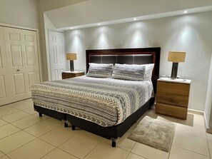 A bedroom with a bed, two nightstands, a door, and a light fixture. - Playa Royale Beachfront Family Condo °BBQ, Terrace & Garden Views° (Nuevo Nayarit)