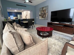 Un salon avec un canapé, une table basse rouge, un téléviseur et, au fond, un coin repas.