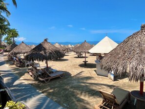 A beachside resort with thatched umbrellas, lounge chairs, and a clear view of the ocean. - Playa Royale Beachfront Family Condo °BBQ, Terrace & Garden Views° (Nuevo Nayarit)