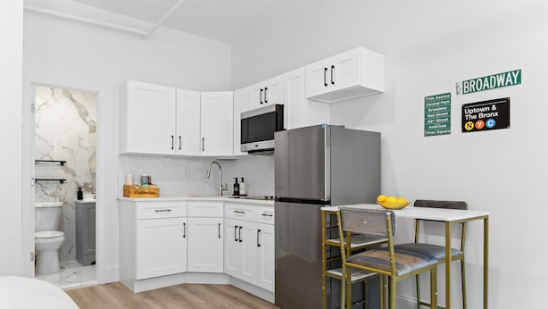 A modern kitchen with white cabinetry, a stainless steel refrigerator, and a bar stool.