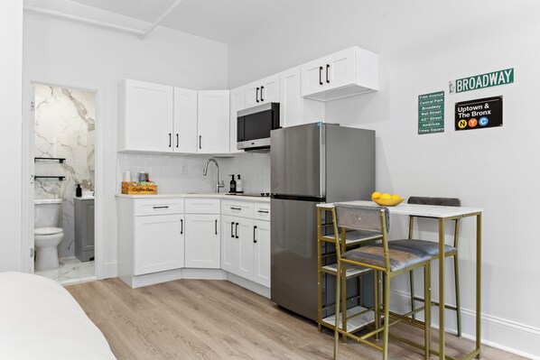 A modern kitchen with white cabinetry, a stainless steel refrigerator, and a bar stool.