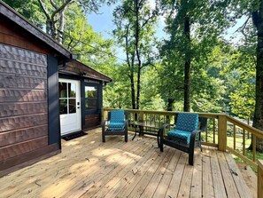 A wooden deck with two chairs and a small building with a door.