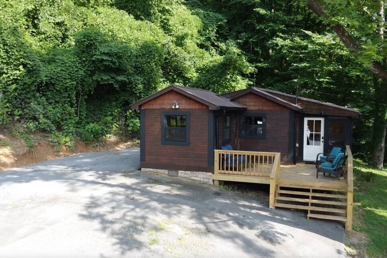 A small cabin with a porch and two chairs, surrounded by trees.