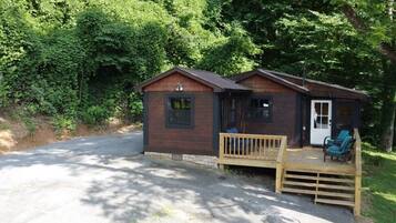 A small cabin with a porch and two chairs, surrounded by trees.