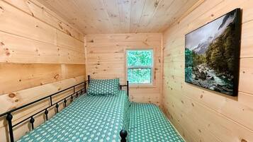 Een houten kamer met twee bedden, een raam en een televisie aan de muur.