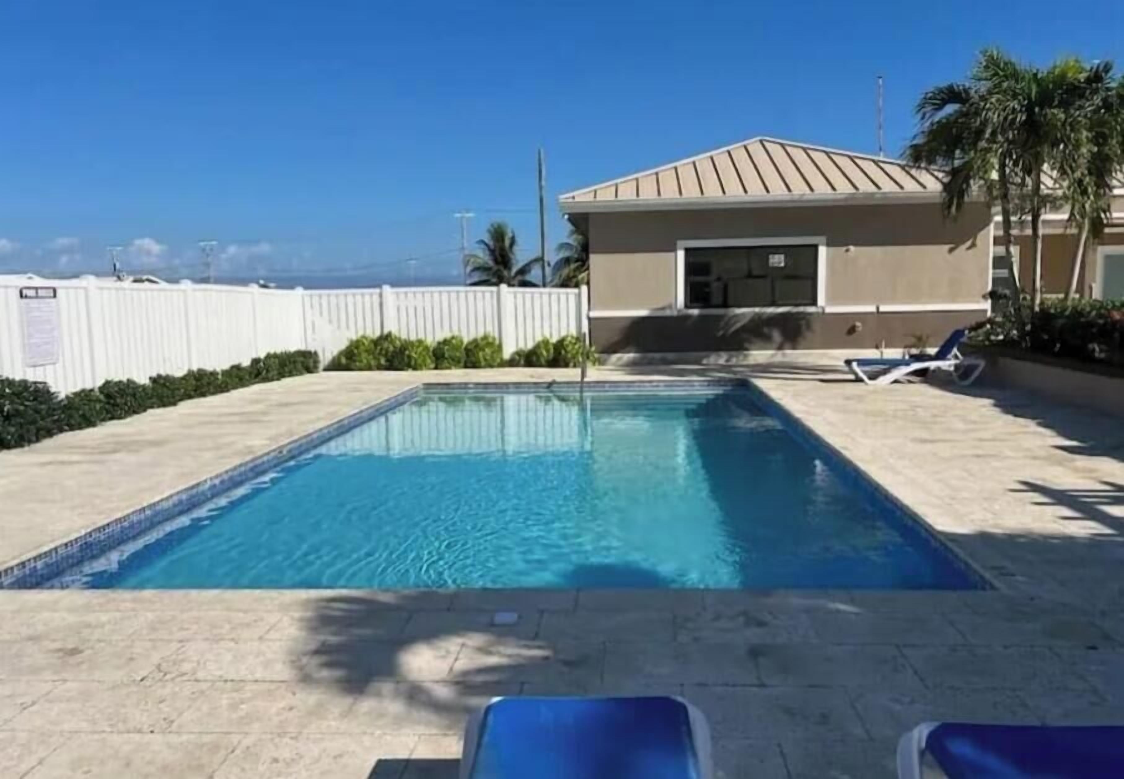 Una piscina amb gandules, un edifici de teulada plana i una tanca blanca.