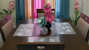 Ein Essbereich mit einem Tisch für vier Personen, einer Vase mit rosa Blumen und Vorhängen in verschiedenen Farben.