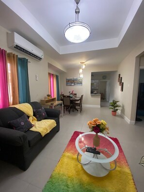 A living room with a black sofa, a coffee table with a vase of flowers, and a dining area in the background. - Cozy 2-bedroom home in charming Lucea with AC, fitness room and pool on property (Lucea)