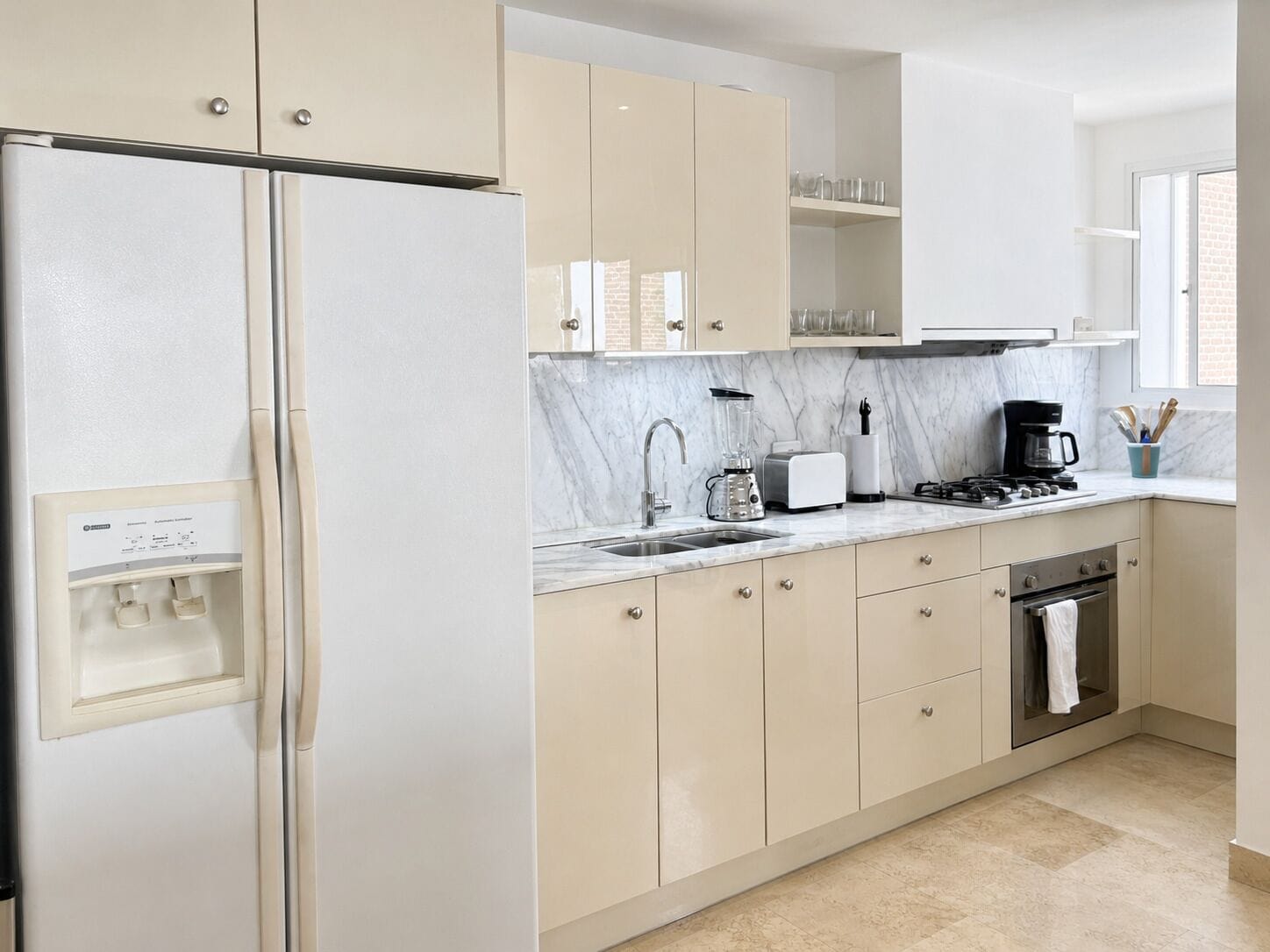 A modern kitchen with a refrigerator, stove, sink, and marble countertop.