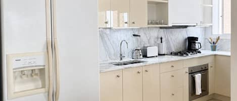 A modern kitchen with a refrigerator, stove, sink, and marble countertop.