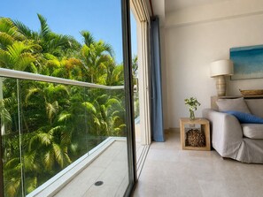 A balcony with a view of lush green foliage, a sofa with cushions, a small table with a vase, and a painting on the wall. - Charming 2-bedroom apartment with AC in Old City Cartagena de Indias (Cartagena de Indias)