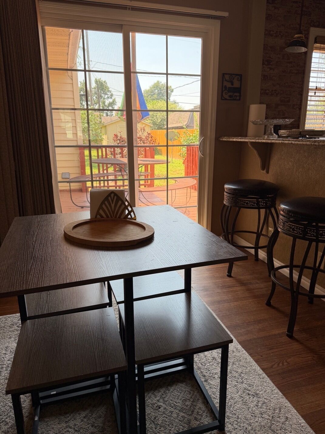 Un coin repas avec une table et des bancs, une vue sur le jardin à travers une porte-fenêtre coulissante, et un espace cuisine avec des tabourets.