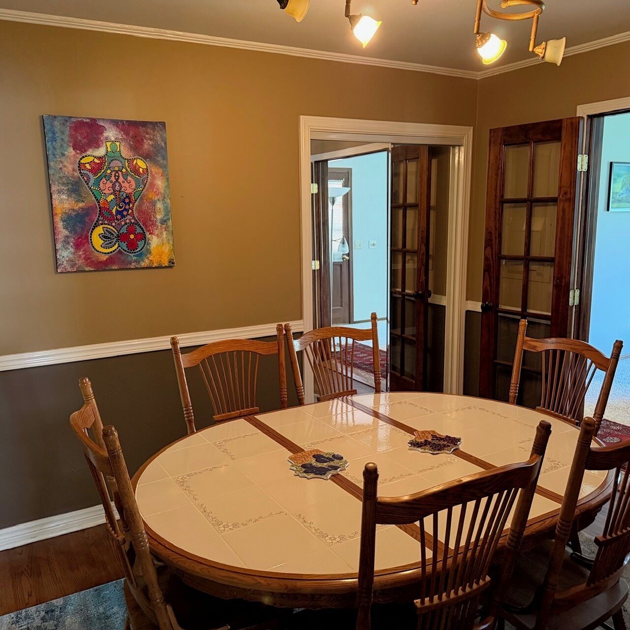 Comedor con una mesa redonda, sillas de madera, un cuadro llamativo y una puerta que da al exterior.