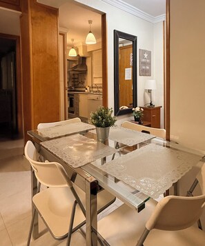 A dining area with a glass table, white chairs, a potted plant, and a kitchen in the background. - A 3 minute walk from the beach
La Piragua Accommodation (Torre del Mar)