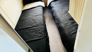 A compact room with two beds, a window with a black blind, and a wooden wardrobe. - Haggerston Castle Caravan Hire West Lawn (Berwick-upon-Tweed)