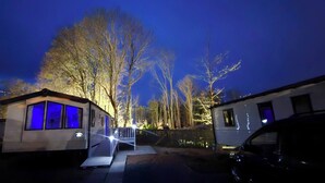 A residential area at night with houses, a small building with blue lighting, and a car parked on the street. - Haggerston Castle Caravan Hire West Lawn (Berwick-upon-Tweed)
