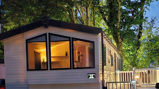Una casa móvil con una amplia sección frontal con ventanas, el número '15' visible y un acceso mediante portón.