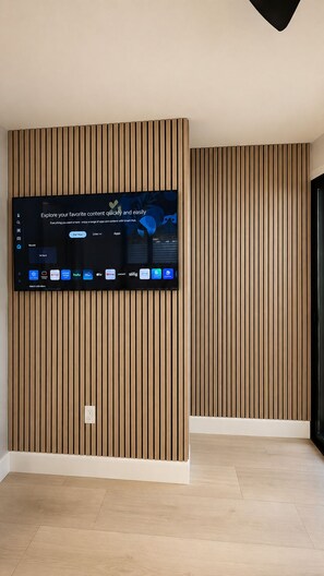 A flat-screen TV mounted on a wall with a wooden panel design. - The Lincoln Luxe Studio• Private Retreat • Midtown • Downtown • Stadium  (Tampa)